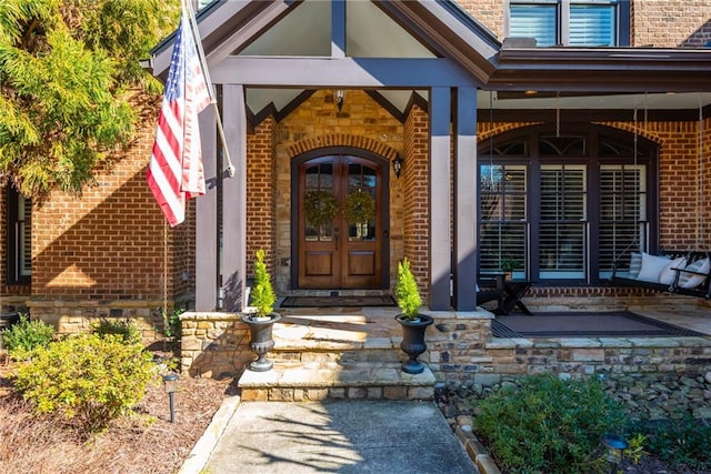 doorway to property with covered porch, french doors, and brick siding