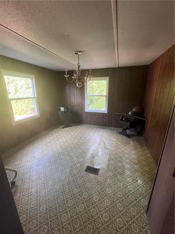 empty room featuring an inviting chandelier, wooden walls, a textured ceiling, and a healthy amount of sunlight