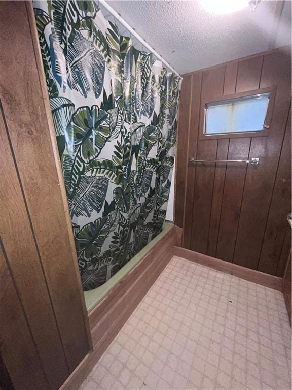 bathroom featuring a textured ceiling, wooden walls, and a shower with shower curtain