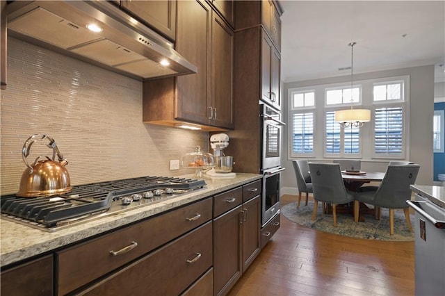 kitchen featuring decorative light fixtures, dark hardwood / wood-style floors, light stone countertops, stainless steel appliances, and ventilation hood