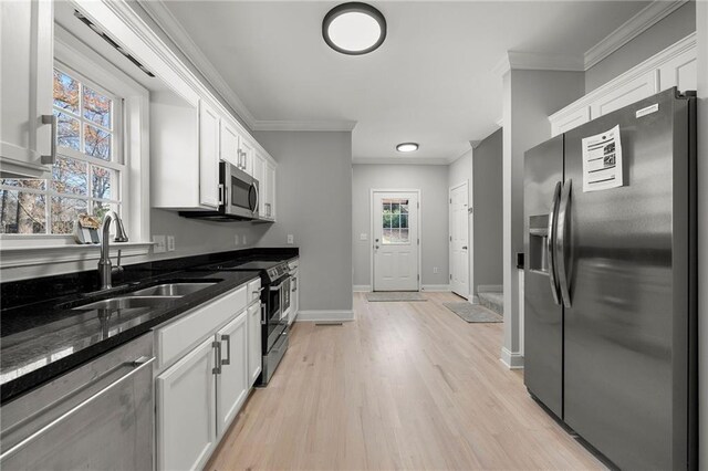 kitchen featuring appliances with stainless steel finishes, crown molding, sink, dark stone countertops, and white cabinetry