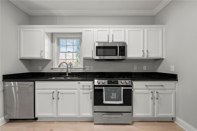 kitchen featuring sink, dark stone countertops, appliances with stainless steel finishes, white cabinets, and ornamental molding