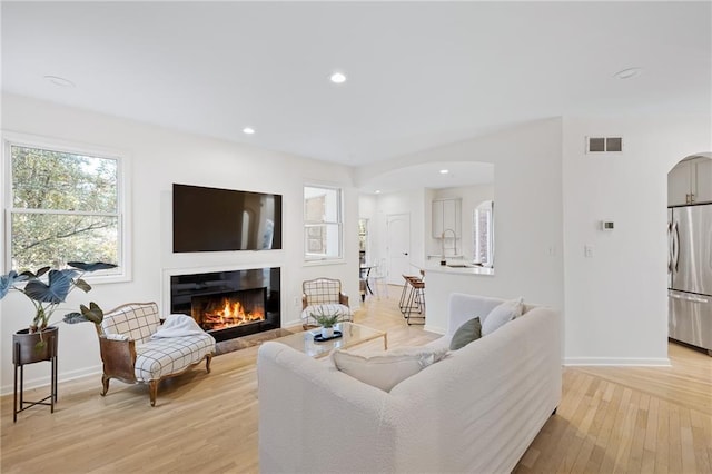 living area featuring visible vents, recessed lighting, arched walkways, a glass covered fireplace, and light wood-type flooring