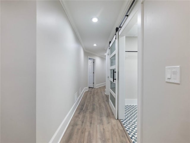 corridor with light hardwood / wood-style floors, ornamental molding, and a barn door