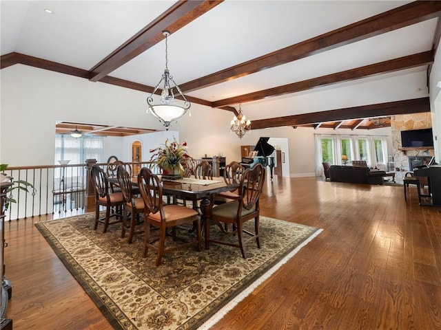 dining area with ceiling fan, dark hardwood / wood-style floors, a stone fireplace, and vaulted ceiling with beams