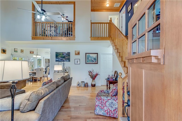 living area featuring wood finished floors, visible vents, a ceiling fan, stairs, and a towering ceiling