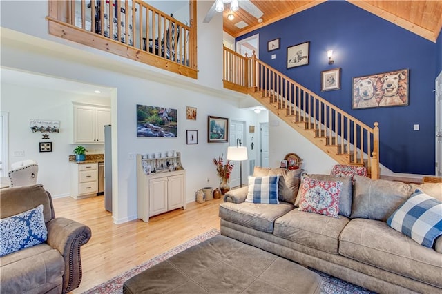 living room with stairway, a ceiling fan, light wood-type flooring, and high vaulted ceiling