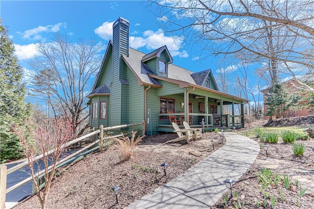 view of side of home with a chimney, covered porch, a ceiling fan, and a shingled roof