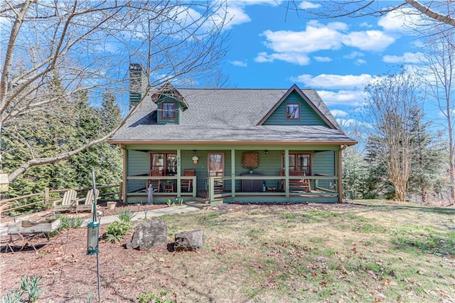 view of front of home with a front lawn, covered porch, a chimney, and a shingled roof