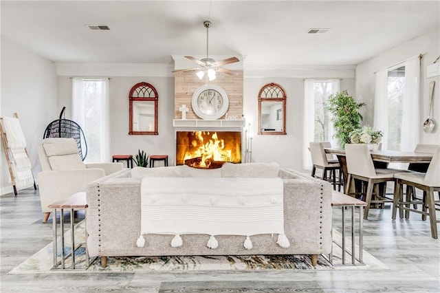 dining room featuring ceiling fan, ornamental molding, a tile fireplace, and light hardwood / wood-style flooring