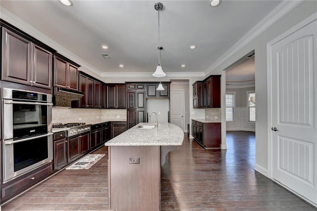 kitchen with sink, appliances with stainless steel finishes, a kitchen island with sink, dark brown cabinetry, and decorative light fixtures