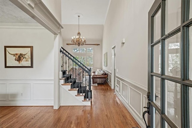 entryway featuring stairway, ornamental molding, wood finished floors, a decorative wall, and a notable chandelier