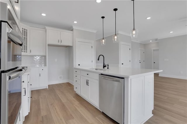 kitchen with stainless steel appliances, light countertops, glass insert cabinets, a kitchen island with sink, and a sink