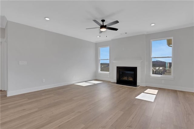 unfurnished living room featuring light wood-style floors, a wealth of natural light, a glass covered fireplace, and baseboards