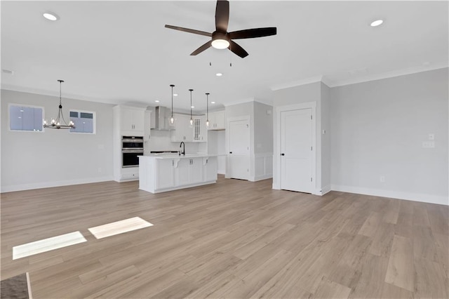 unfurnished living room featuring ceiling fan with notable chandelier, light wood-style floors, recessed lighting, and crown molding