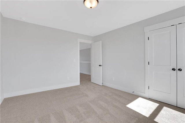 unfurnished bedroom featuring baseboards, a closet, and light colored carpet