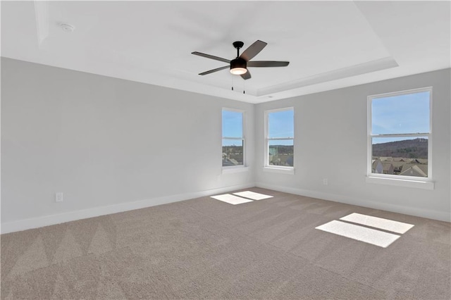 carpeted spare room with a raised ceiling, ceiling fan, and baseboards