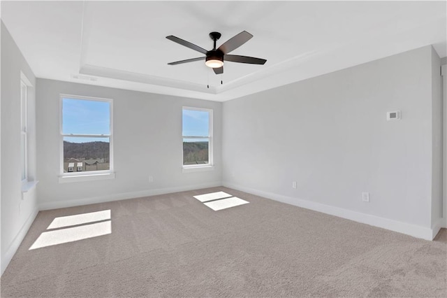 empty room with a raised ceiling, light colored carpet, and baseboards