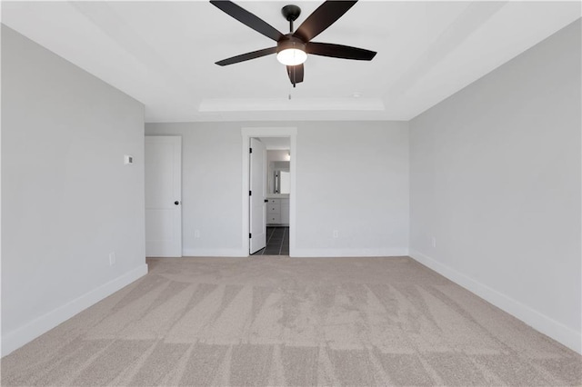 spare room with light carpet, baseboards, a raised ceiling, and a ceiling fan