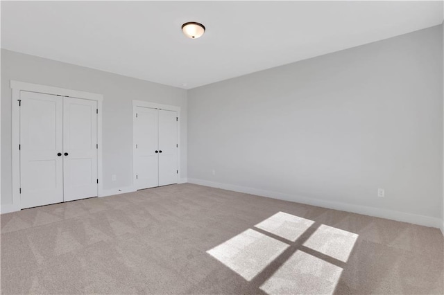 unfurnished bedroom featuring light carpet, baseboards, and multiple closets