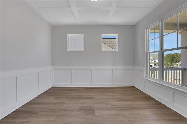 unfurnished room with light wood-type flooring, a wainscoted wall, coffered ceiling, and a decorative wall