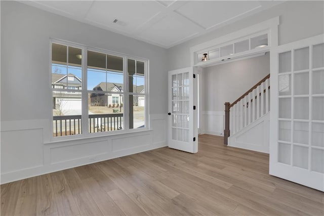 entryway with coffered ceiling, a wainscoted wall, light wood-style flooring, stairway, and a decorative wall