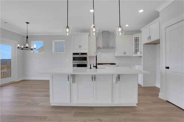 kitchen with wall chimney exhaust hood, glass insert cabinets, a kitchen island with sink, light countertops, and pendant lighting