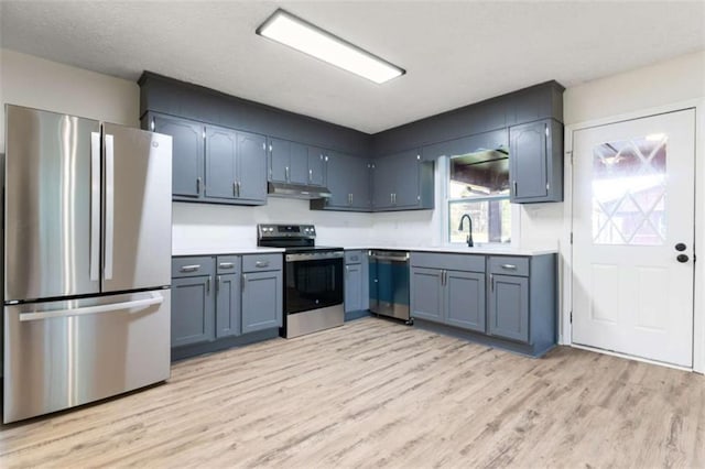 kitchen with a sink, light wood-style flooring, stainless steel appliances, light countertops, and under cabinet range hood
