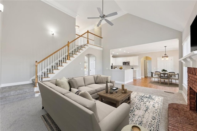 living room with a fireplace, light carpet, ceiling fan with notable chandelier, and high vaulted ceiling