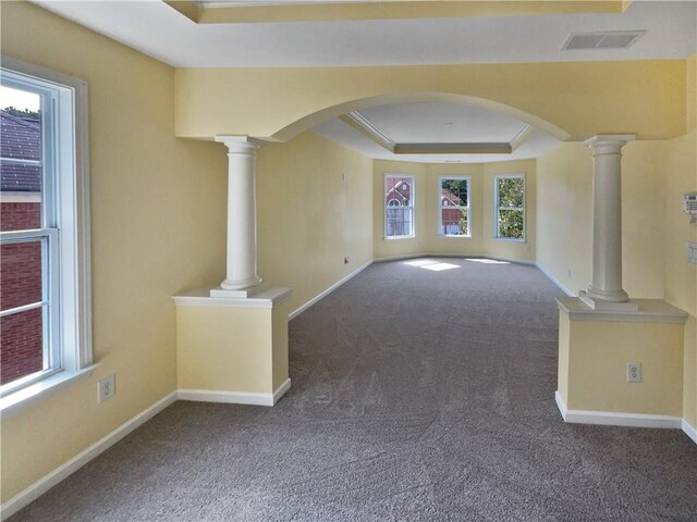 unfurnished living room with arched walkways, decorative columns, a raised ceiling, visible vents, and baseboards