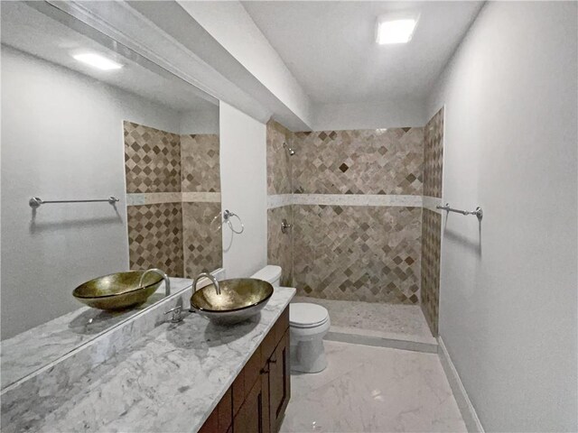 bathroom with baseboards, toilet, marble finish floor, a tile shower, and vanity