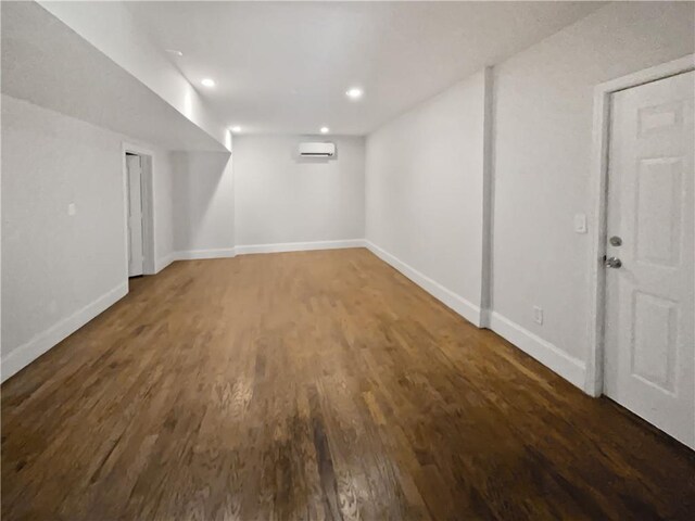 finished below grade area featuring dark wood-style floors, an AC wall unit, recessed lighting, and baseboards