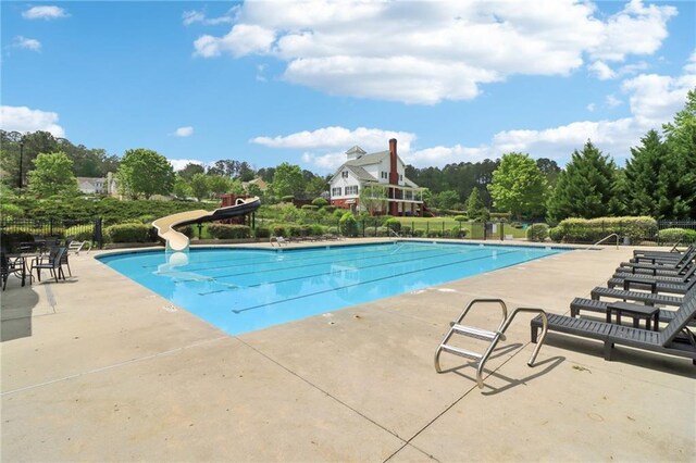 community pool with fence, a water slide, and a patio