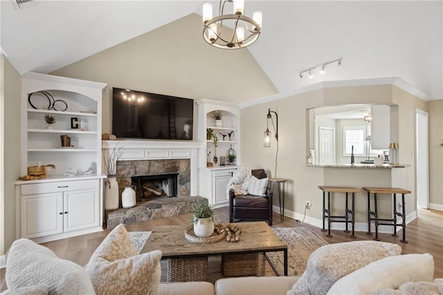 living room with hardwood / wood-style floors, vaulted ceiling, built in features, and a stone fireplace