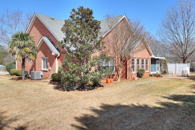 rear view of property with a yard, brick siding, cooling unit, and fence