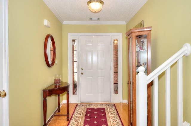 entryway with light wood finished floors, crown molding, visible vents, and a textured ceiling