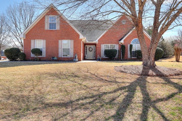 view of front of house featuring roof with shingles, a front lawn, and brick siding