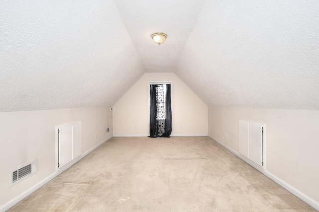 bonus room featuring baseboards, visible vents, light colored carpet, lofted ceiling, and a textured ceiling