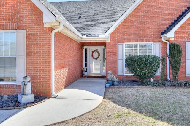 doorway to property with roof with shingles and brick siding