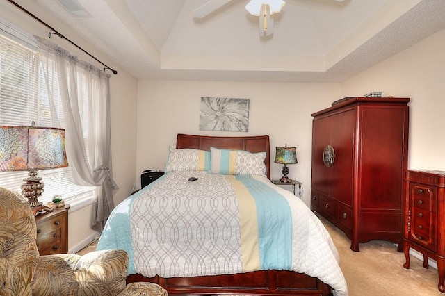 bedroom with light carpet, ceiling fan, visible vents, and a raised ceiling