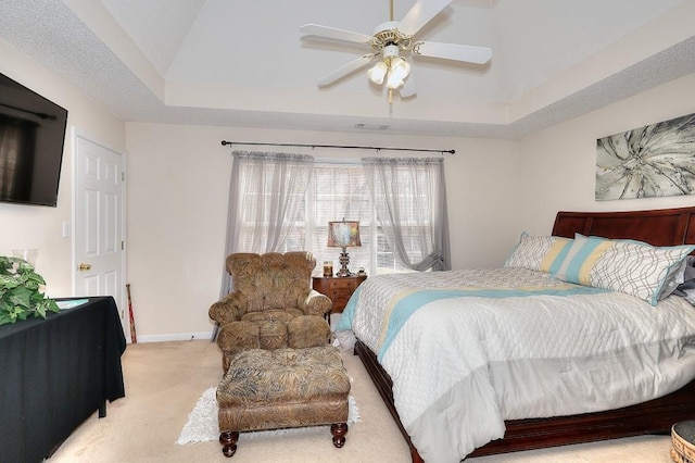 bedroom featuring light carpet, a ceiling fan, visible vents, baseboards, and a tray ceiling