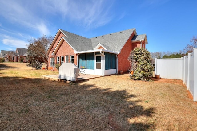 back of house featuring a sunroom, fence, a yard, a patio area, and brick siding