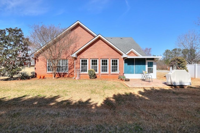 rear view of house with a patio, brick siding, fence, a sunroom, and a lawn