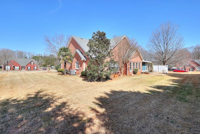 exterior space featuring a front lawn, central AC, fence, and brick siding