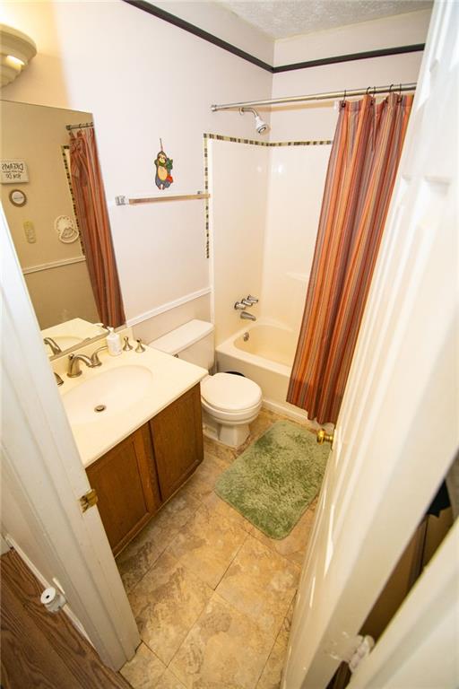 full bathroom with toilet, a textured ceiling, vanity, and shower / bath combination with curtain