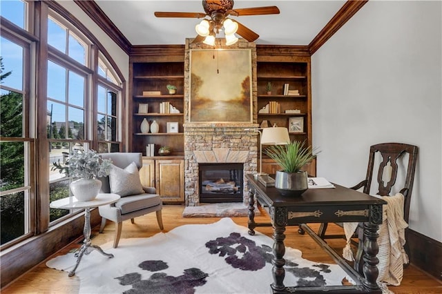 sitting room with a stone fireplace, crown molding, built in shelves, and wood finished floors