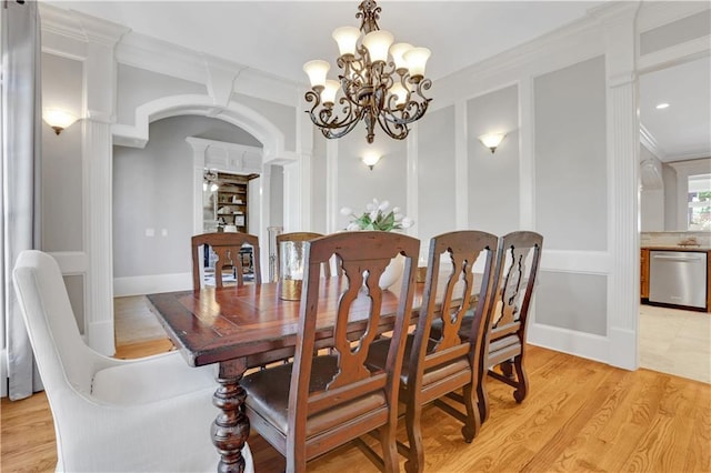 dining area featuring ornate columns, light wood finished floors, an inviting chandelier, arched walkways, and crown molding