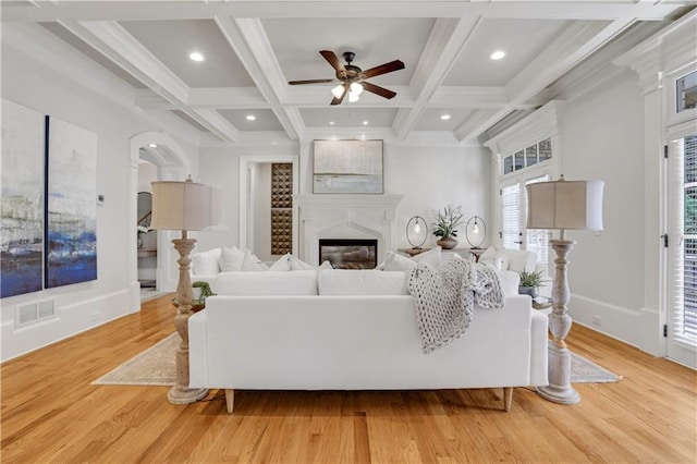 living area featuring visible vents, beam ceiling, light wood-style flooring, coffered ceiling, and a glass covered fireplace
