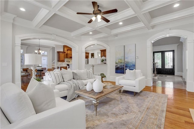 living room featuring beamed ceiling, coffered ceiling, french doors, arched walkways, and light wood finished floors