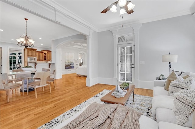 living room featuring light wood finished floors, crown molding, baseboards, ceiling fan with notable chandelier, and arched walkways